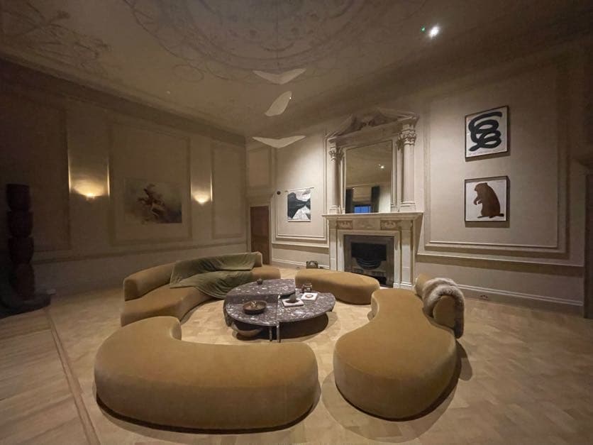 Elegant lounge area with curved sofas, a marble coffee table, and artwork on the walls, featuring a decorative fireplace.