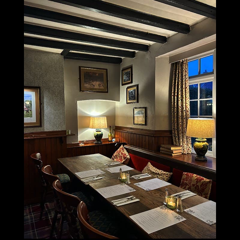 Cozy bar interior with wooden beams, a long table set for dining, warm lighting, and decorative wall art.
