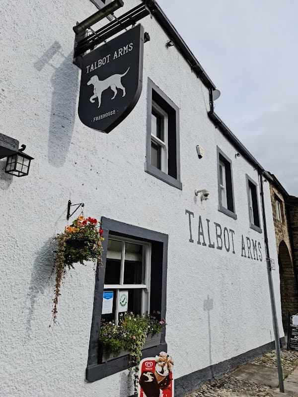 White-washed exterior of Talbot Arms pub, featuring a dog sign, window boxes with flowers, and a cobblestone entrance.